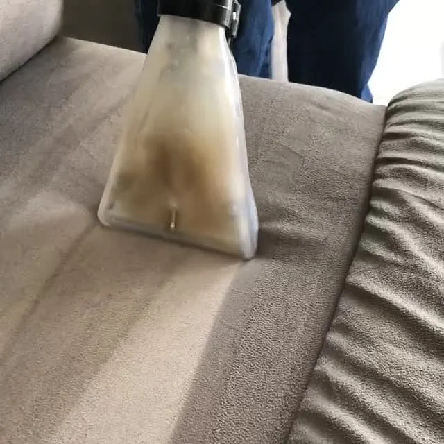 O bico de extração transparente passando no assento de um sofá e puxando a água suja.